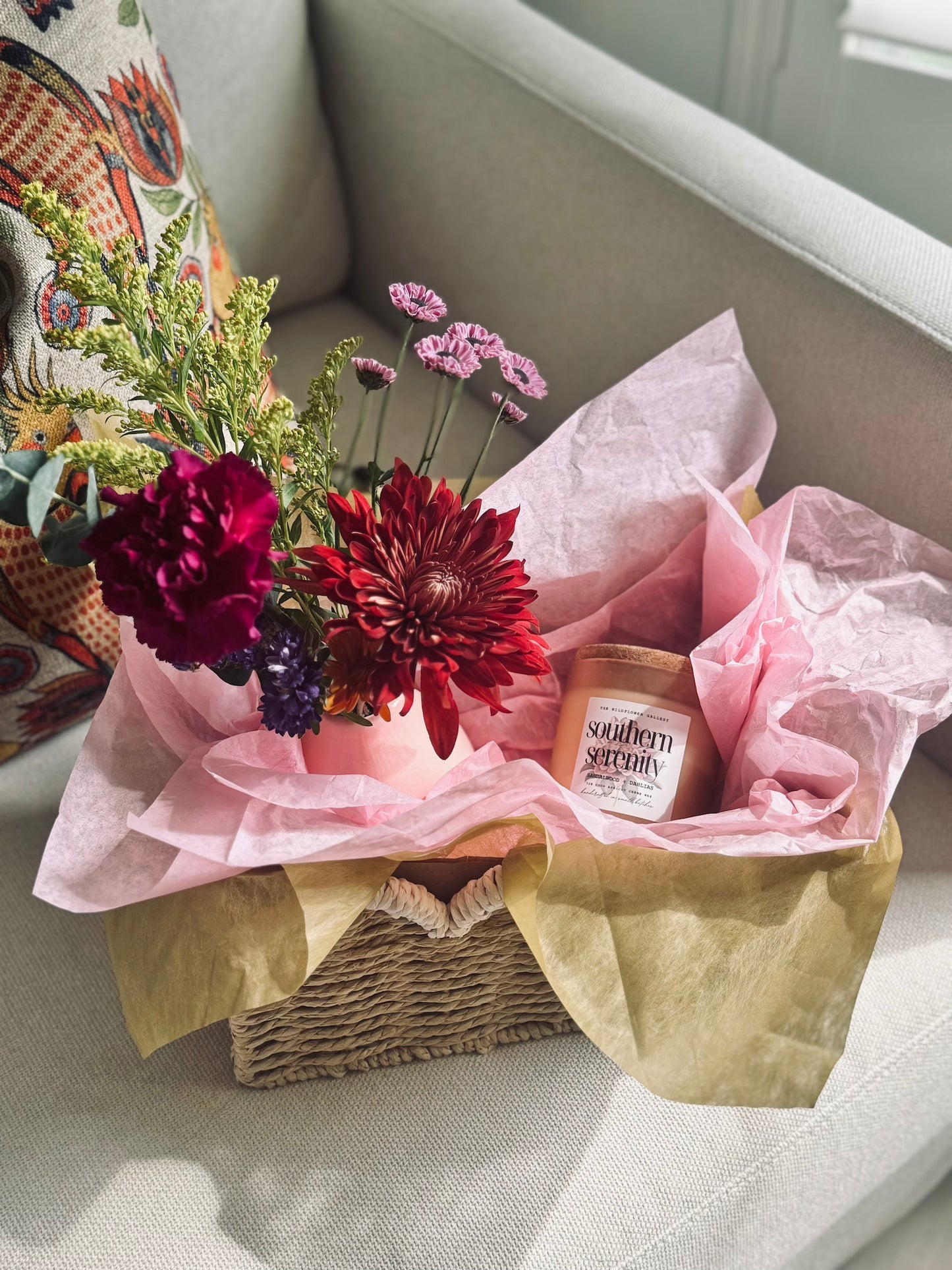 Fresh floral arrangement and non-toxic coconut apricot wax candle inside The Wildflower Gallery Bloom Basket – artisanal gift for local delivery in Texas.