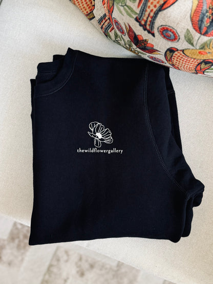 Folded black crewneck sweatshirt by The Wildflower Gallery – sustainably made from organic cotton and ethically produced for comfort and mindful style.